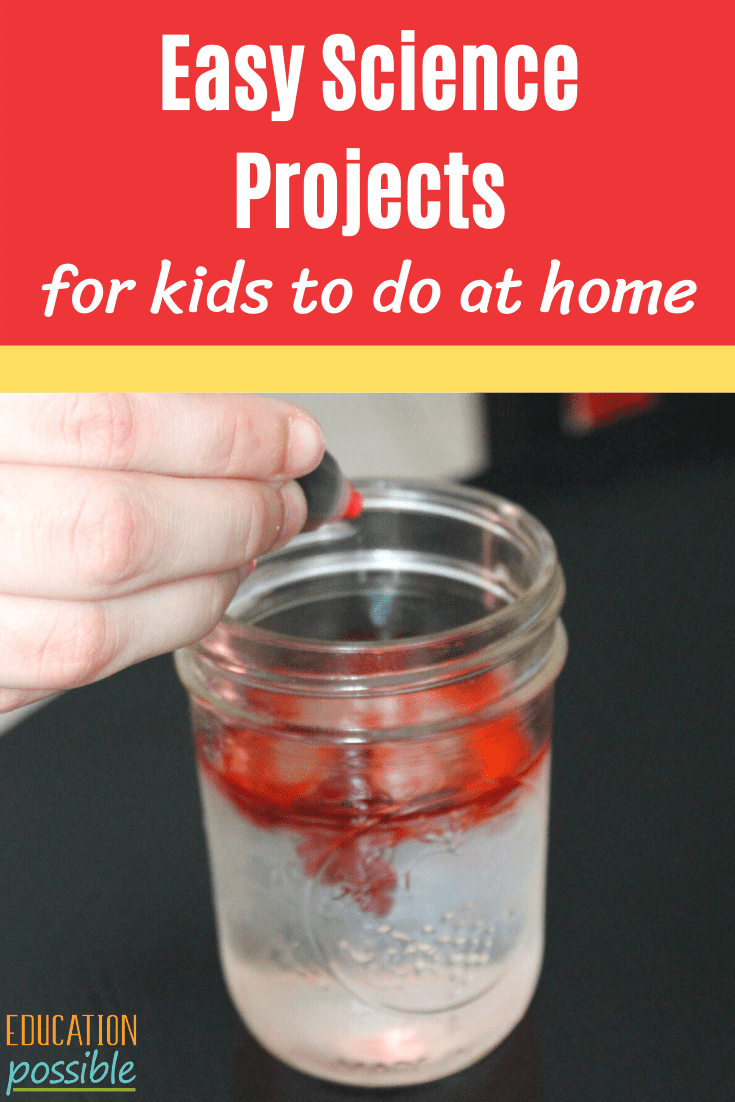 Hand squeezing red food coloring into a small glass jar full of water, the red coloring is starting to color the water in the jar. A red text box is at the top with white text reading easy science projects for kids to do at home.