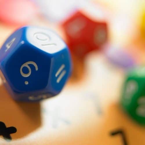 Blue colored multi-sided math die, red and green ones blurred in the background