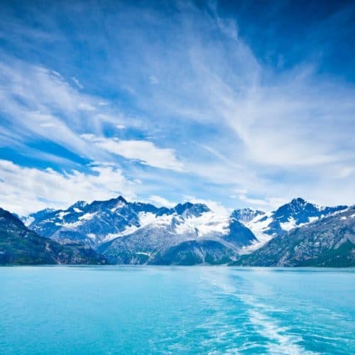 Crystal blue water with snow capped mountains in background, blue sky in Alaska