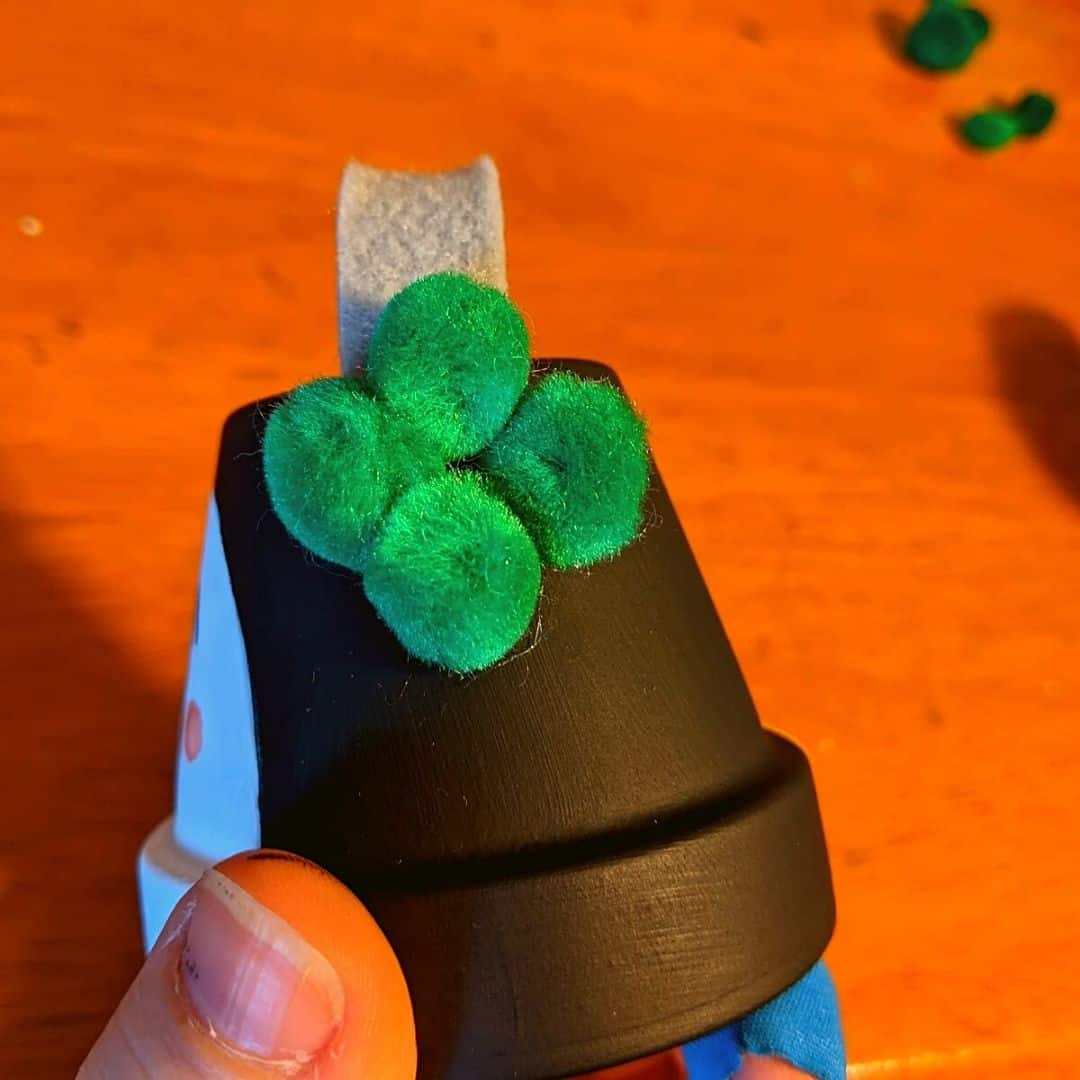 4 green craft pom poms as earmuffs on mini clay pot penguin craft.