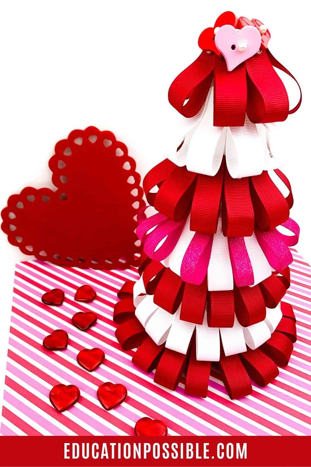 DIY red and white Valentine's Day ribbon tree on striped paper and red hearts around it.