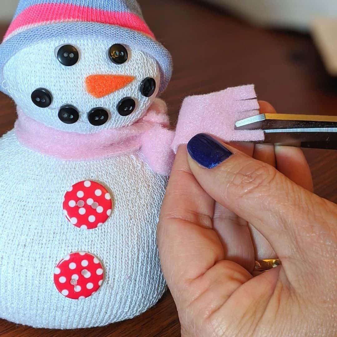 Sock snowman craft, hands holding scissors, cutting fringe on end of fleece scarf.