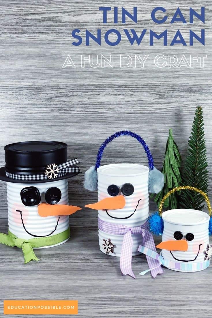 Three tin can snowmen - a DIY craft - standing next to two small green evergreen trees on a tabletop.