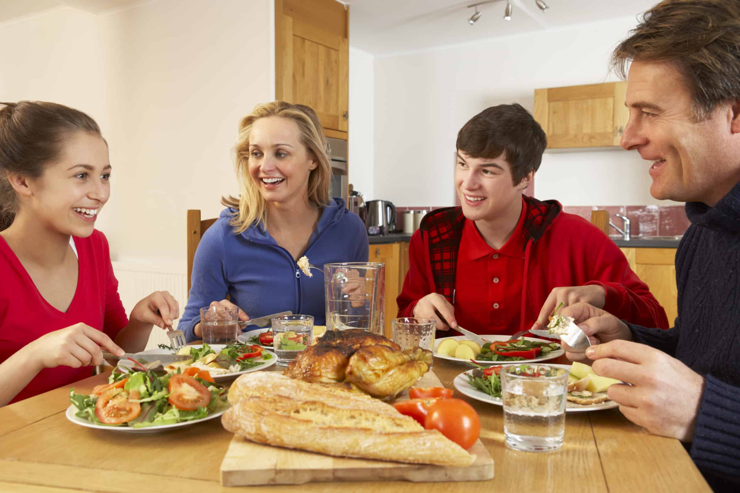Teen girl and boy with family eating dinner at dining room table.