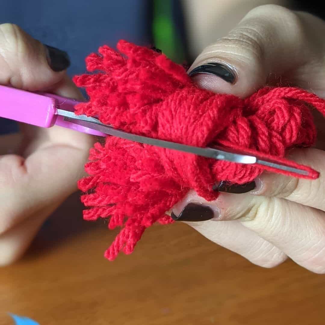 Girl cutting loops of red yarn to make a pom pom.