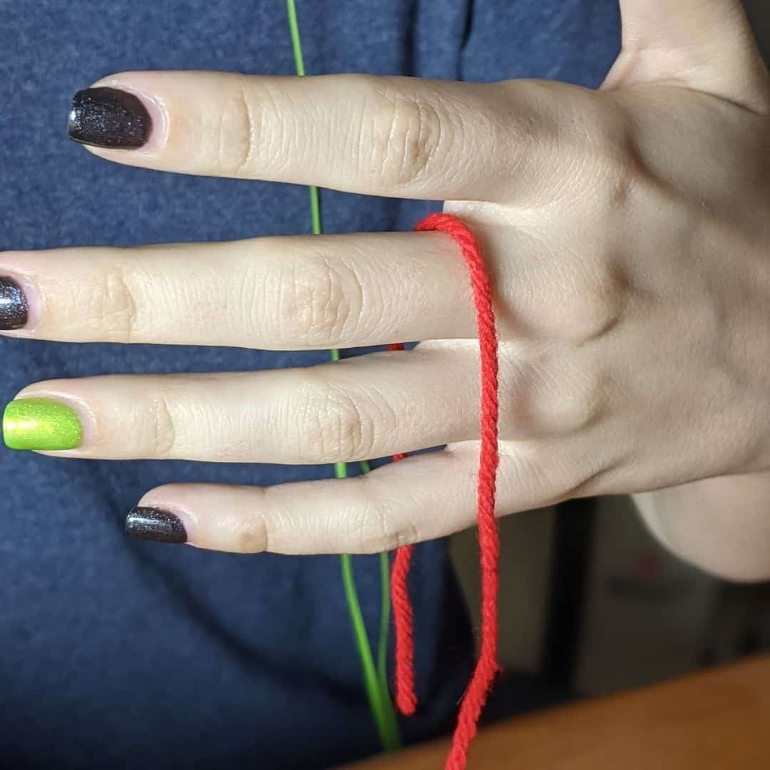 Girl with a red piece of yarn hanging between her first two fingers.