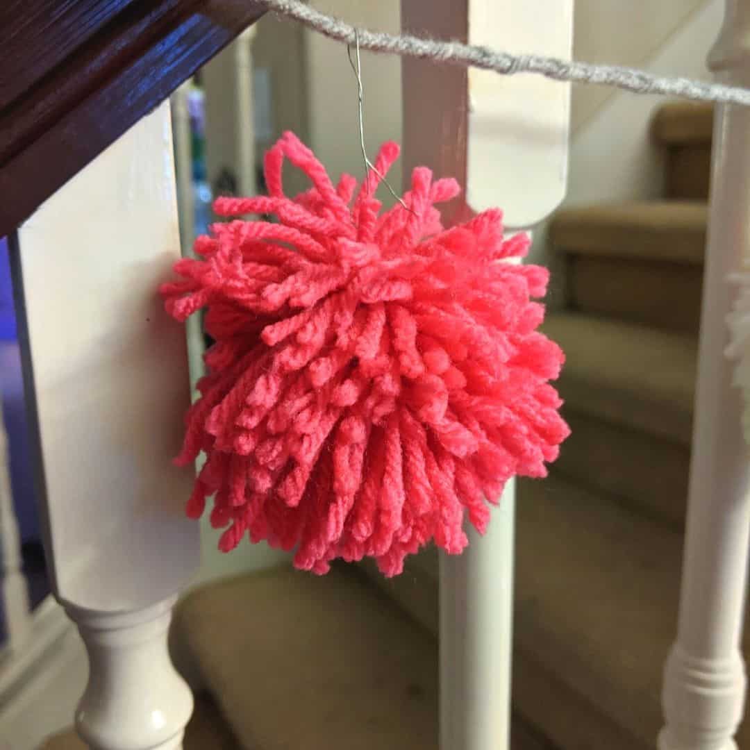 pink yarn pom-pom on grey braided garland hanging on railing