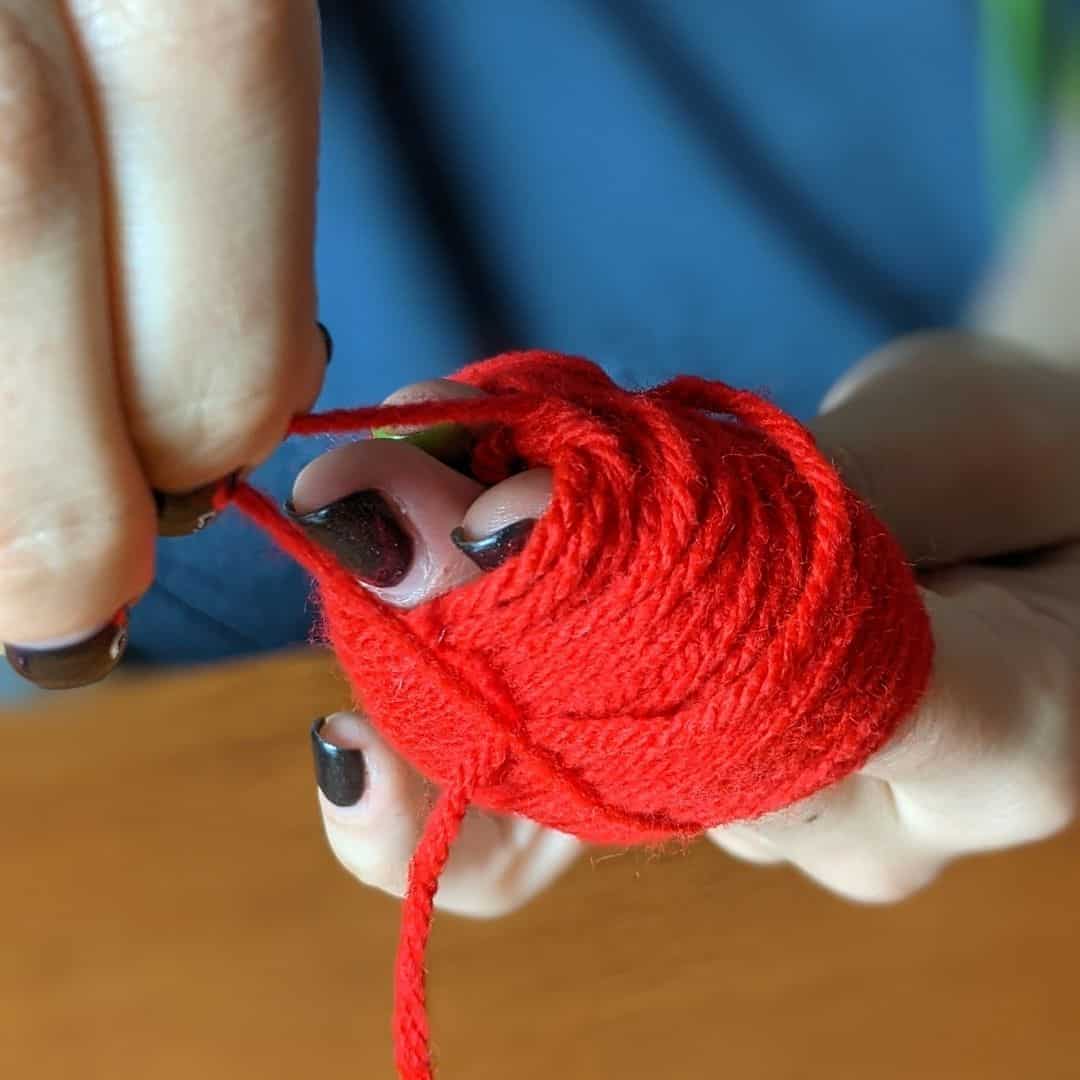 Girl wrapping red yarn around her first two fingers.