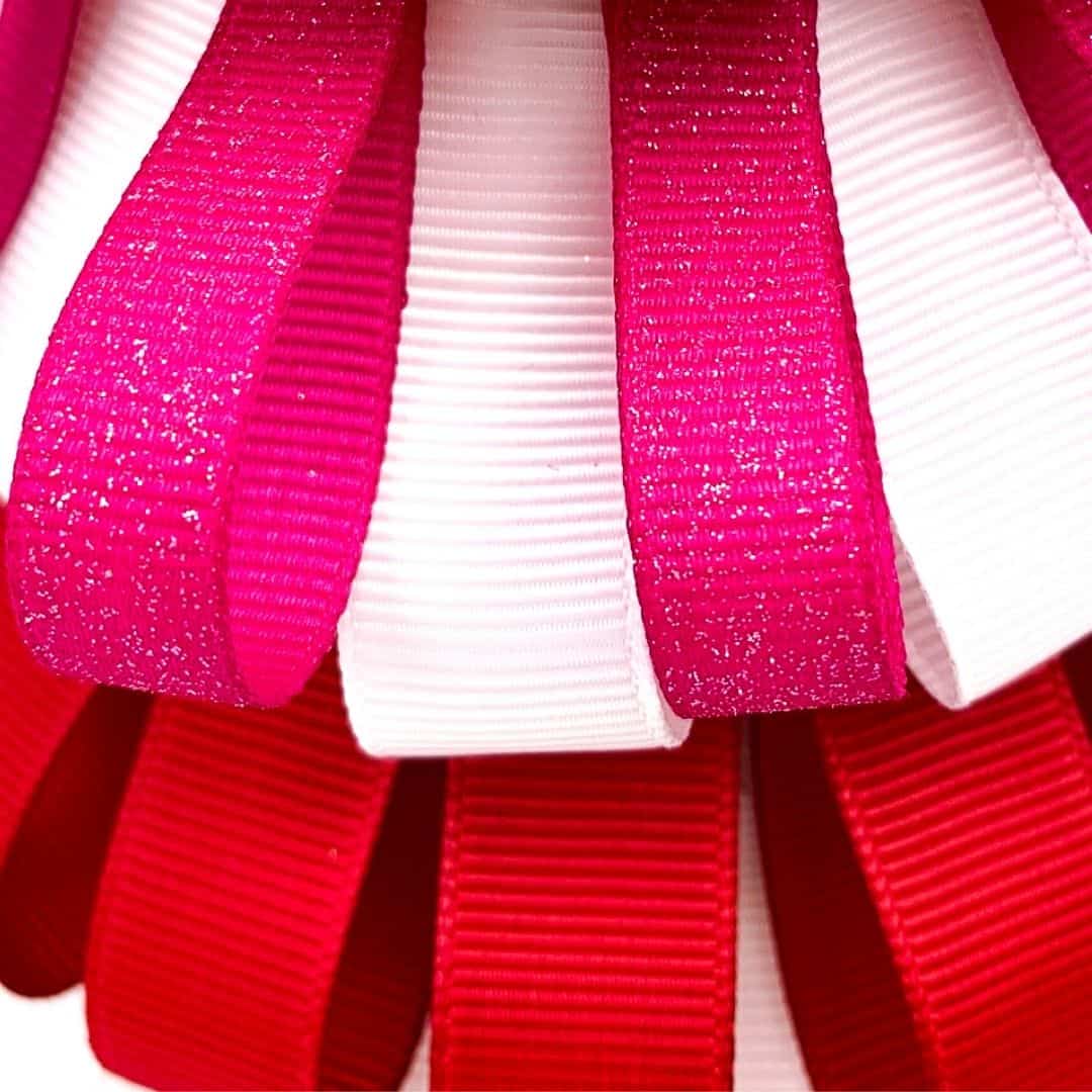 Red. white, and pink ribbon loops circling around a Styrofoam cone.