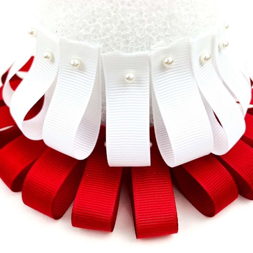 A row of red ribbon loops and a row of white ribbon loops above them pinned to a Styrofoam cone.
