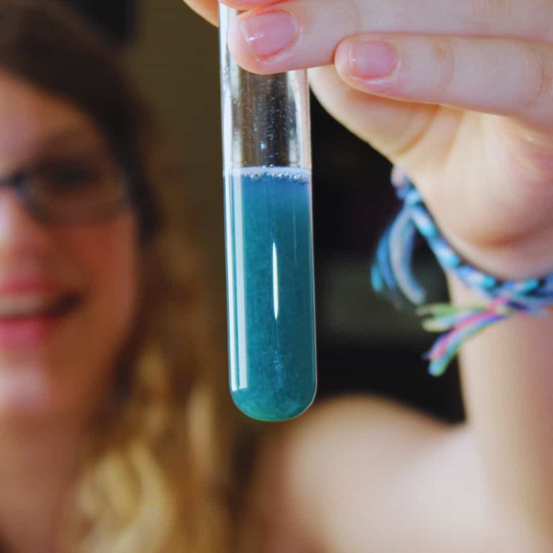 Teen girl holding a test tube with blue liquid inside.