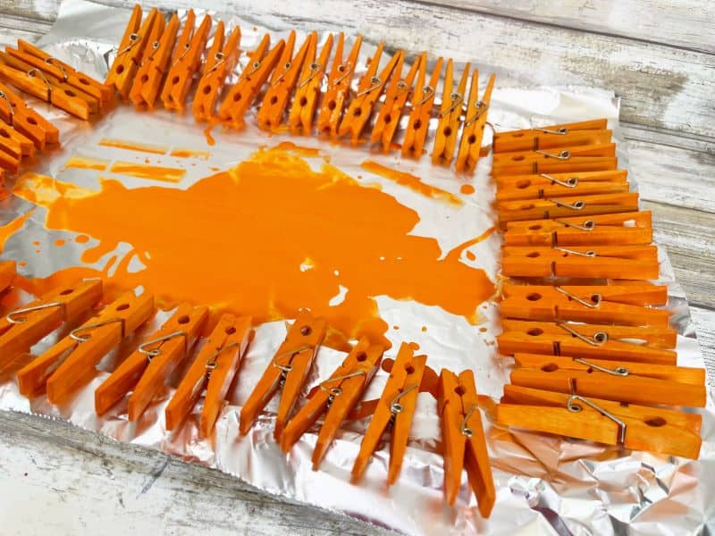 Clothespins have been painted orange and are sitting on foil to dry.