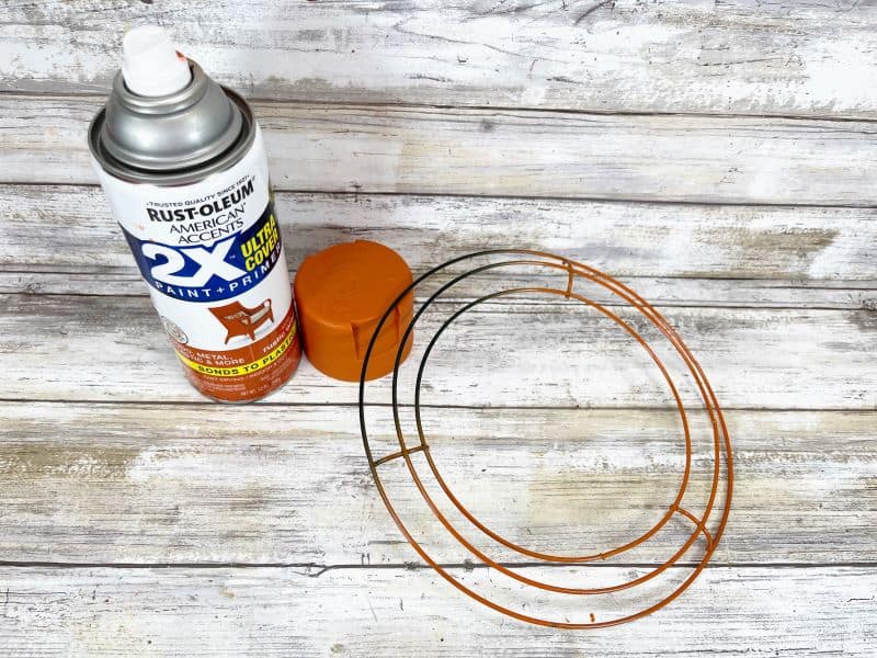 Spray painting a wire wreath orange as part of a fall craft.