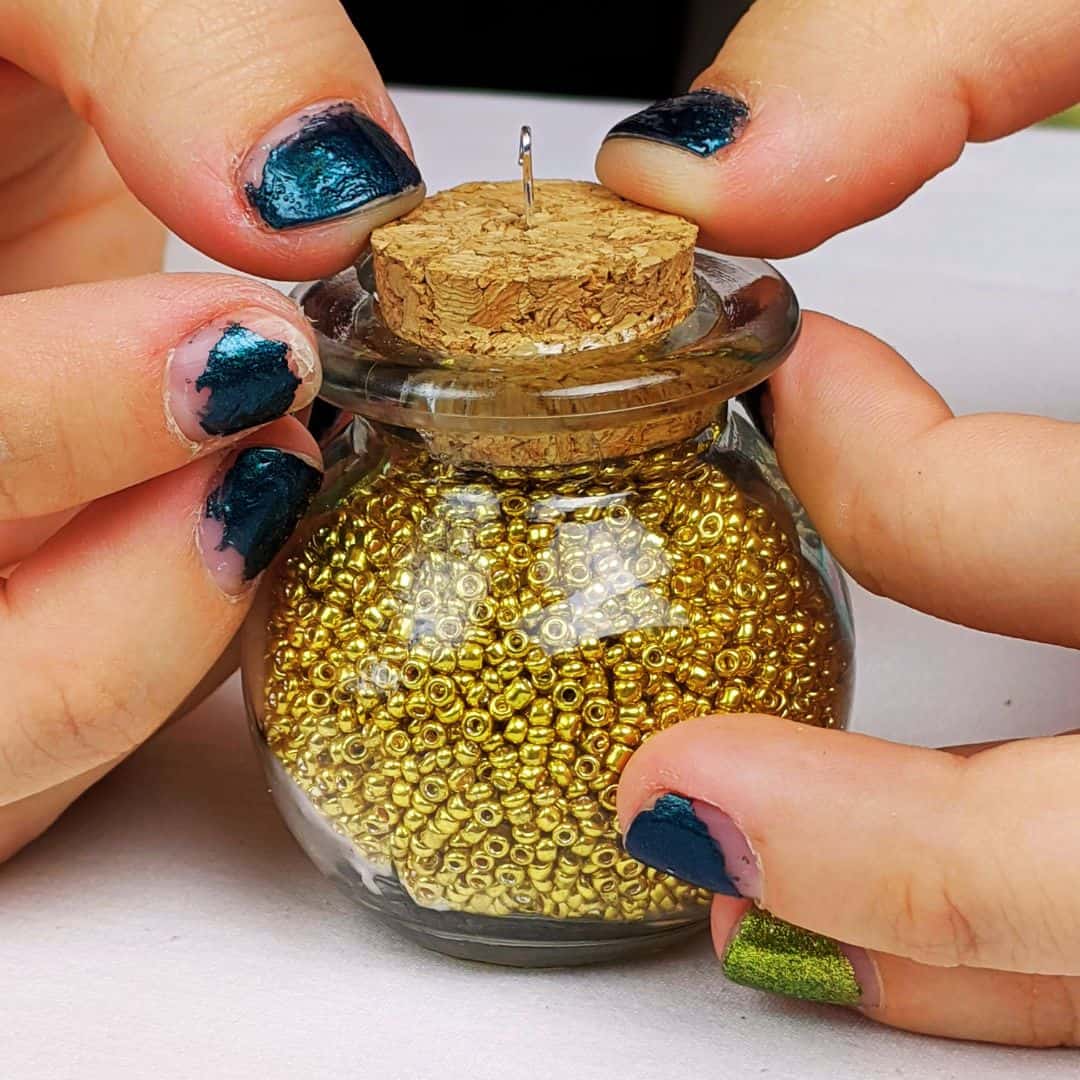 Teen girl pressing a cork top down into a glass jar filled with gold beads