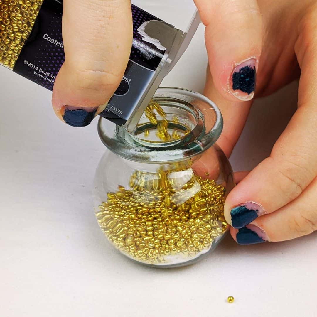 Teen girl pouring small gold beads into a small glass jar