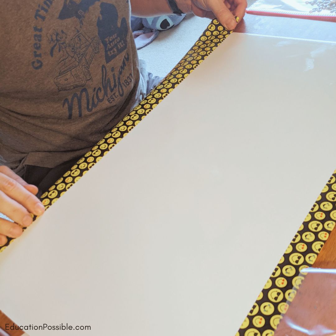Man adding emoji patterned Duck Tape to the long edge of a white board.