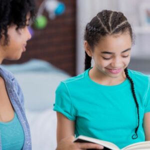 African American mom and tween daughter homeschooling, reading a book