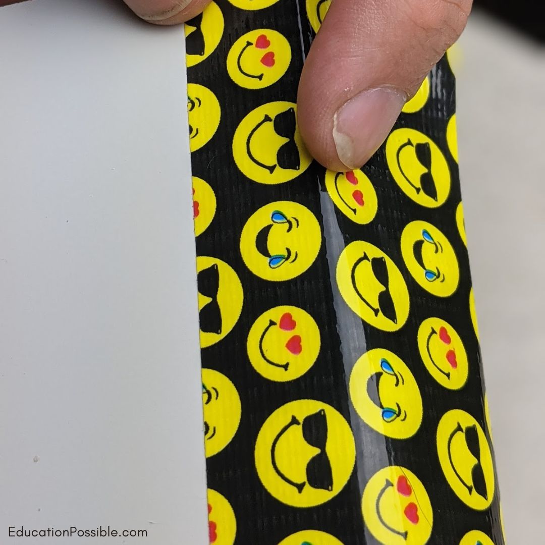 Man folding emoji patterned Duct Tape over the edge of a white board