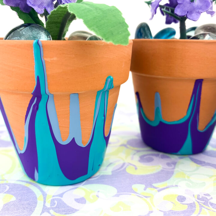 2 Terra cotta pots with blue and purple paint dripped from the bottom. Purple silk flower inside with glass beads.