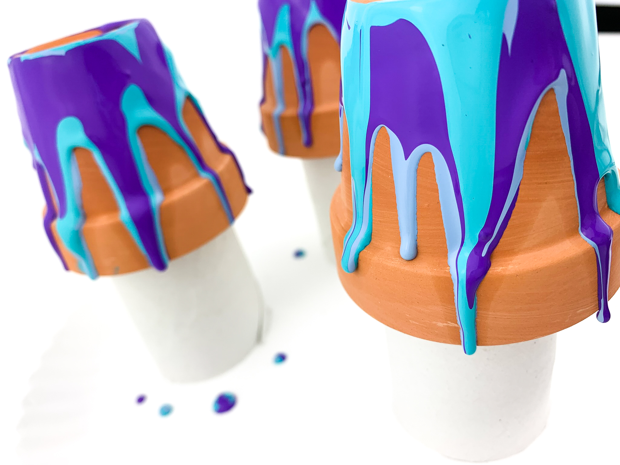 3 mini clay pots upside down, sitting on toilet paper rolls. Blue and purple paint dripping down the sides.
