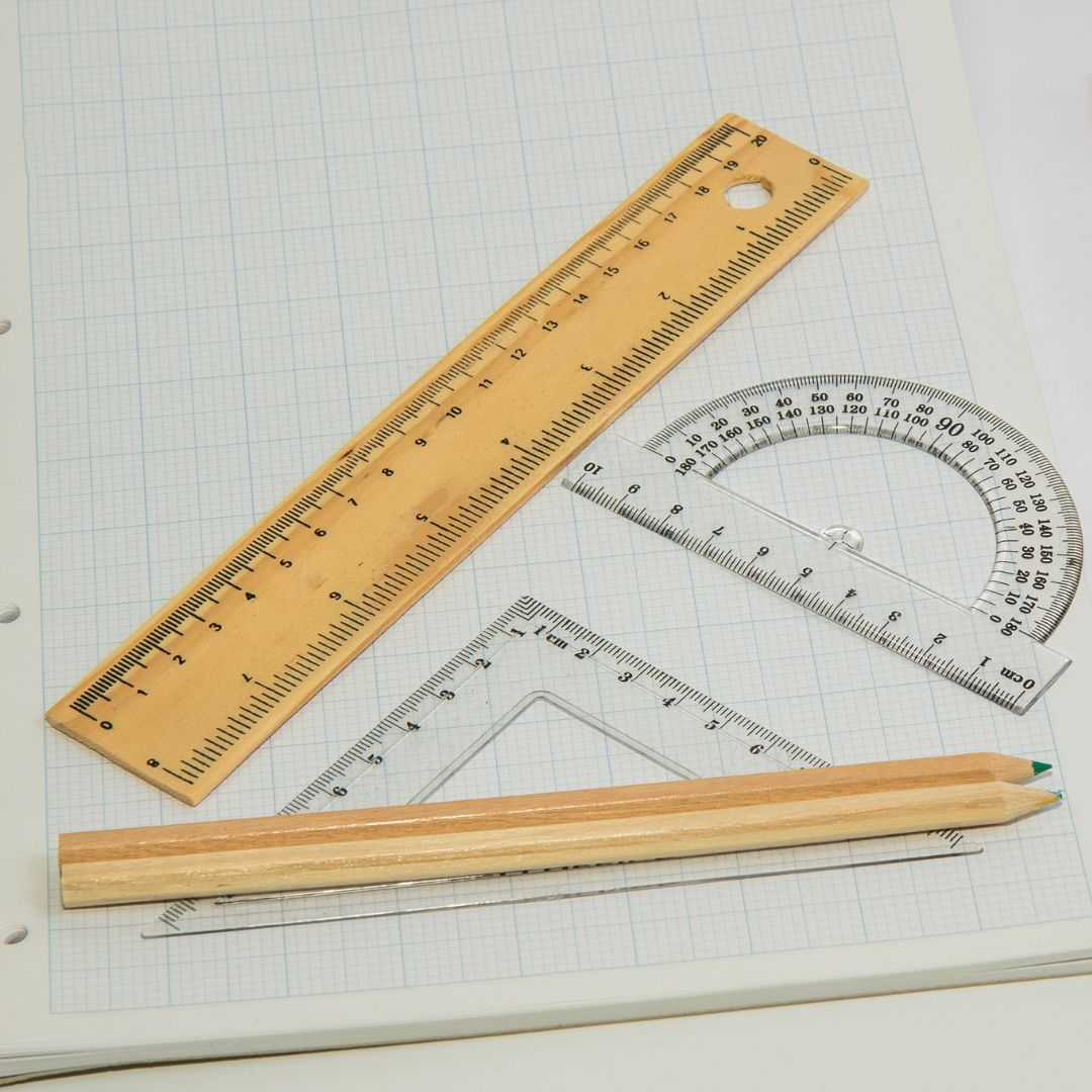 Math tools and pencils sitting on tablet of graph paper. Ruler, triangle, protractor.