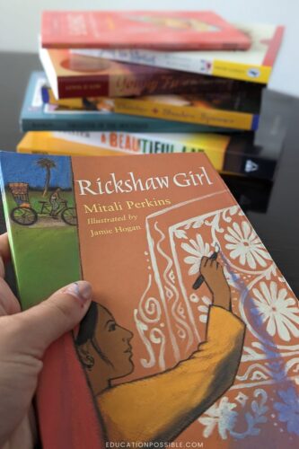 Girl holding Rickshaw Girl book with other Eastern Hemisphere middle grade books in a staggered stack in the background.